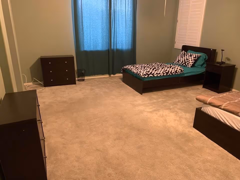 Bedroom with two single beds, dark wood furniture, teal curtains and beige carpet.