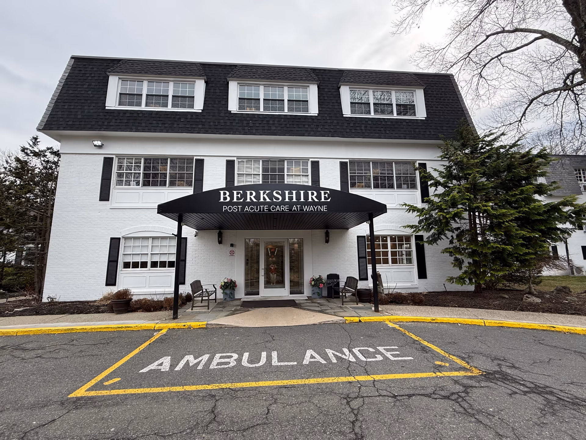 White three-story care facility with a black awning over the entrance and ambulance marking