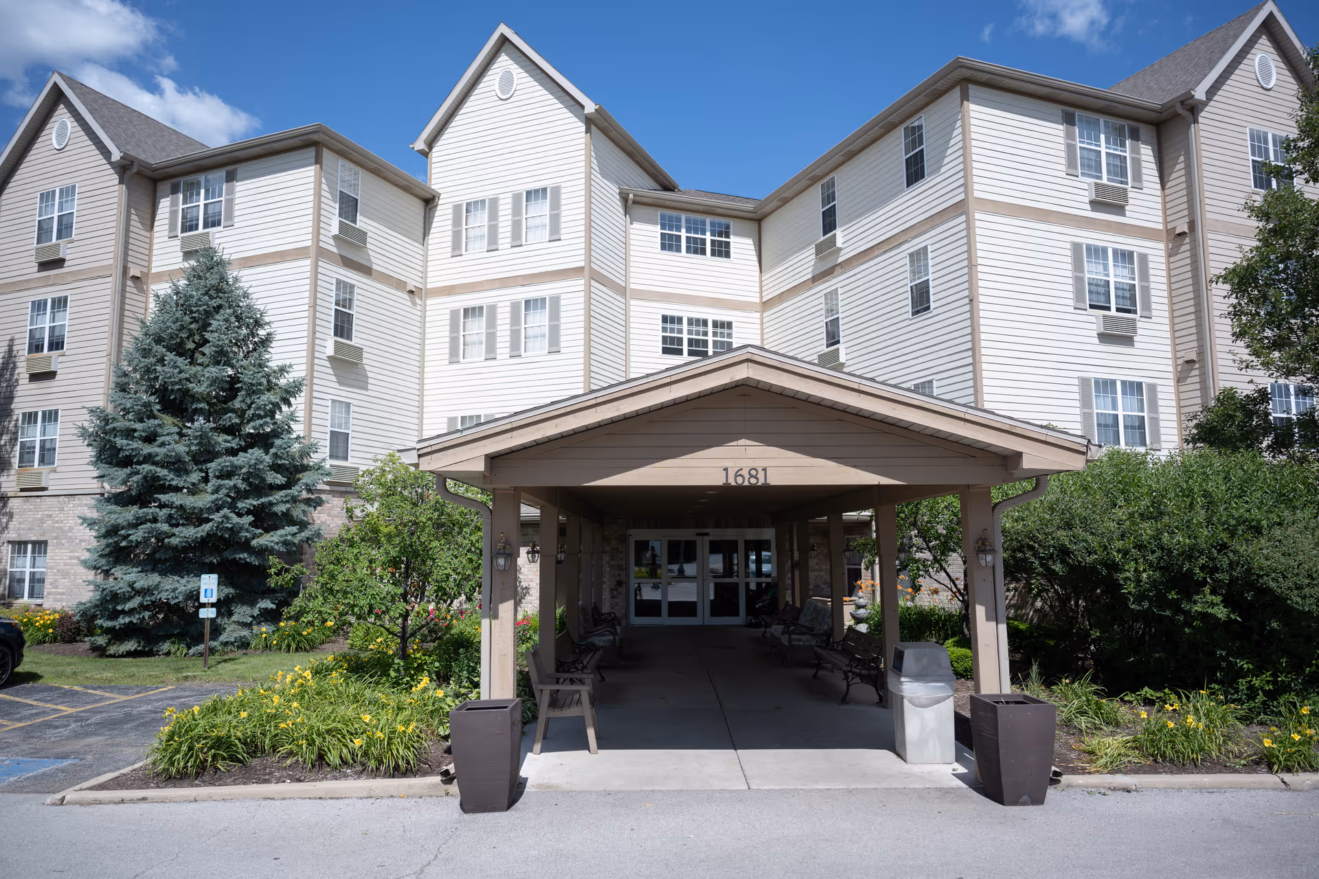 Front entrance of a multi-story senior living building with a covered porte-cochere labeled 1681 and landscaped grounds.