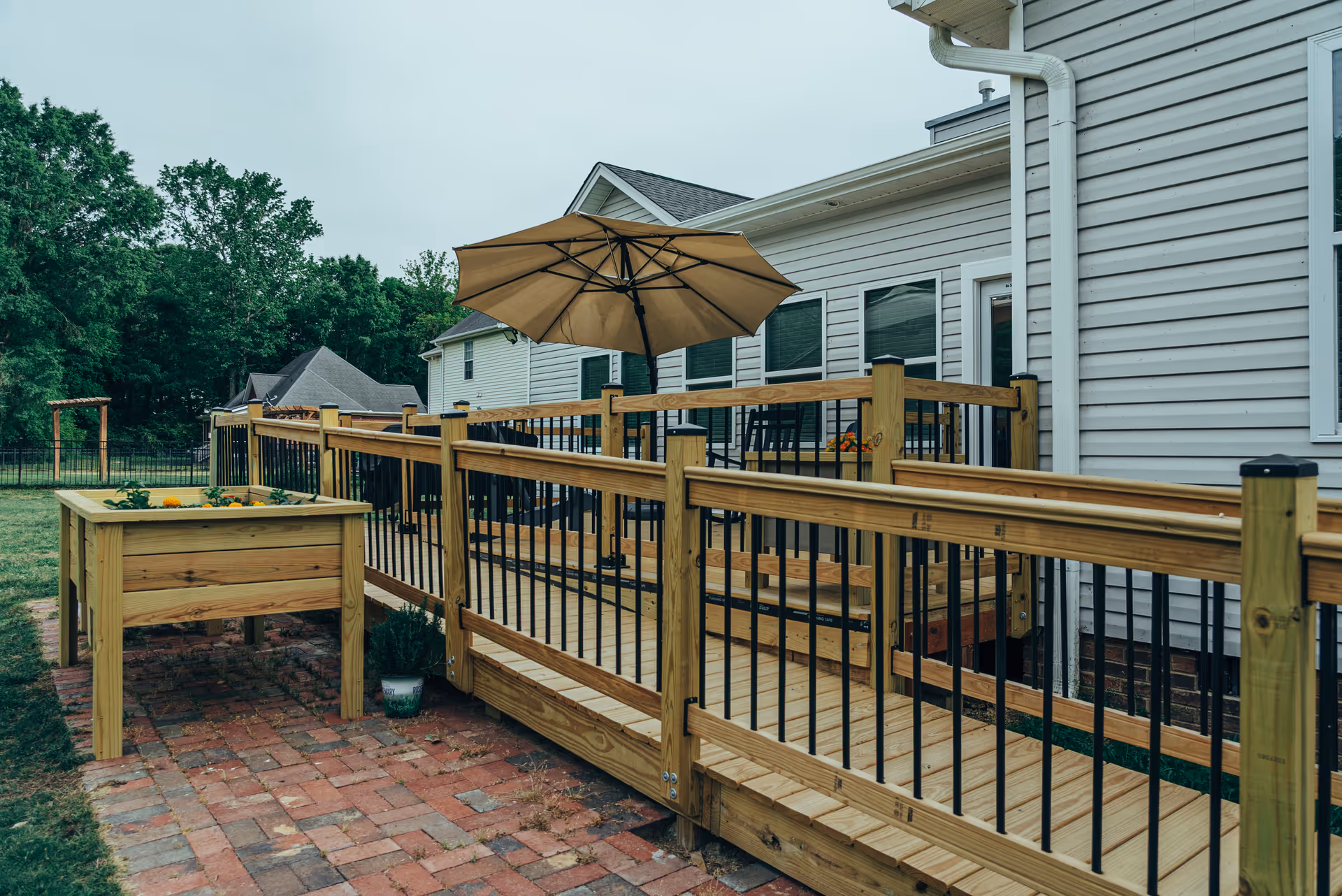 Wooden deck with umbrella, railings, and chairs extending from a light-colored house.