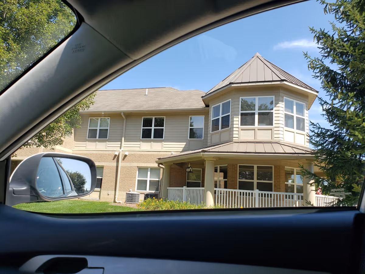 Front exterior view of a retirement facility with a porch, seen from a car.