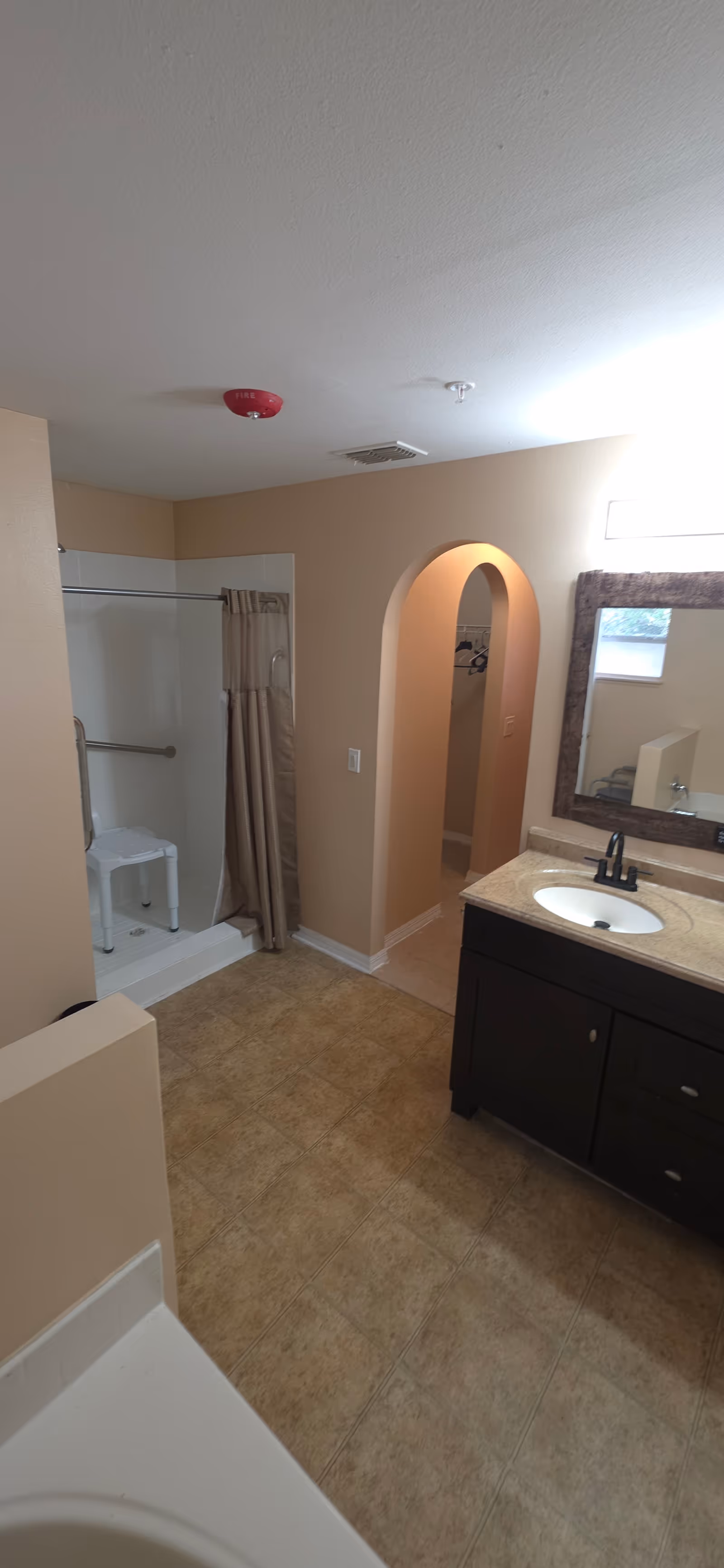 Beige bathroom with shower, curtain, stool, sink vanity, and arched doorway.