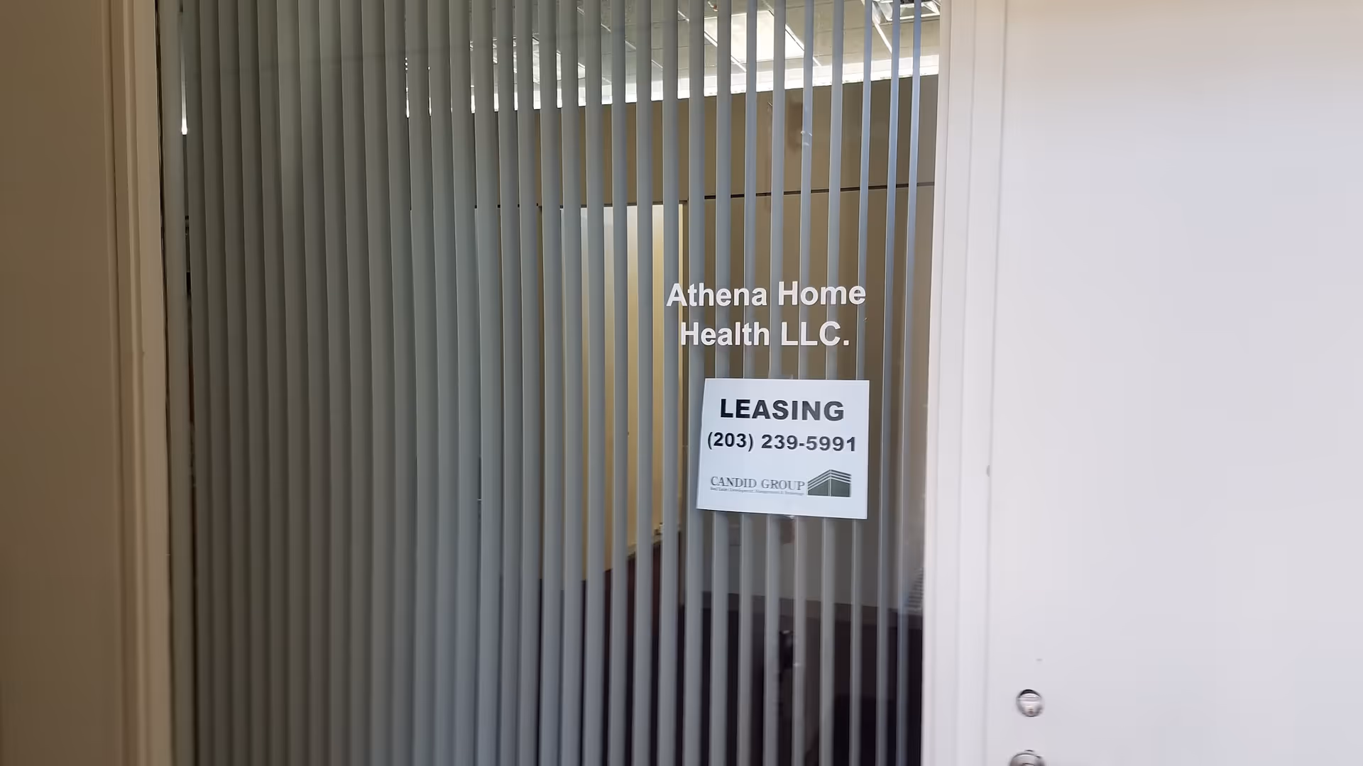 Interior glass door with vertical blinds displaying Athena Home Health LLC and a leasing sign.