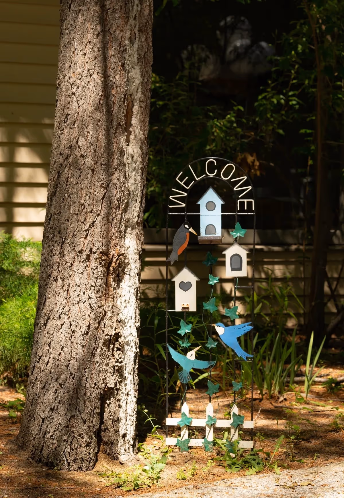 Colorful welcome sign with birdhouses beside a tree outside a building.