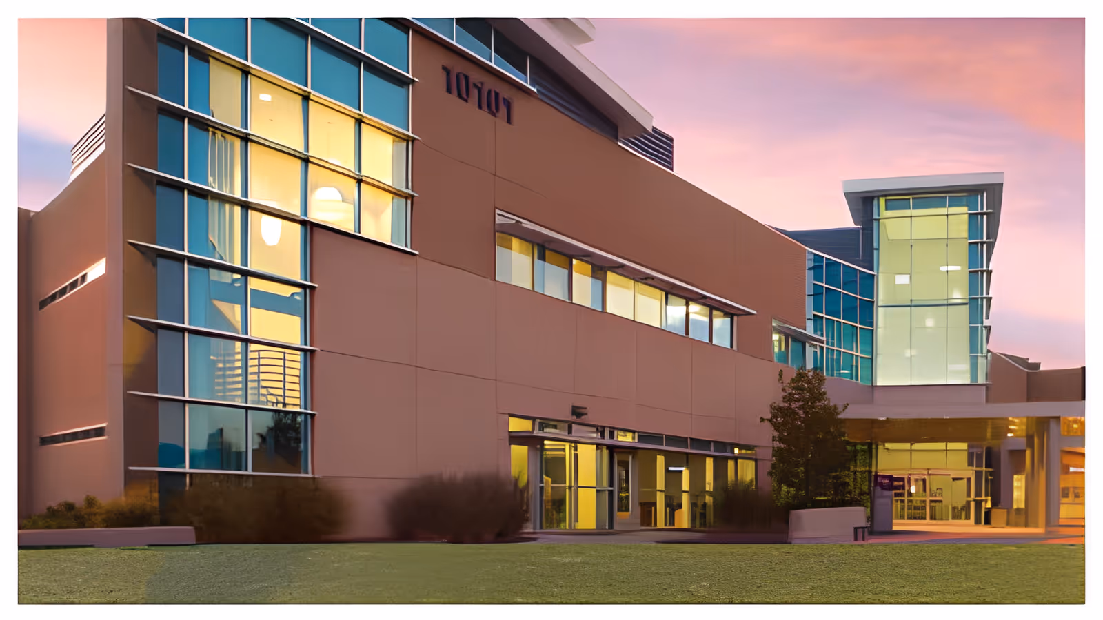 Exterior view of a modern assisted living facility building at dusk with large glass windows and a well-maintained lawn in front.