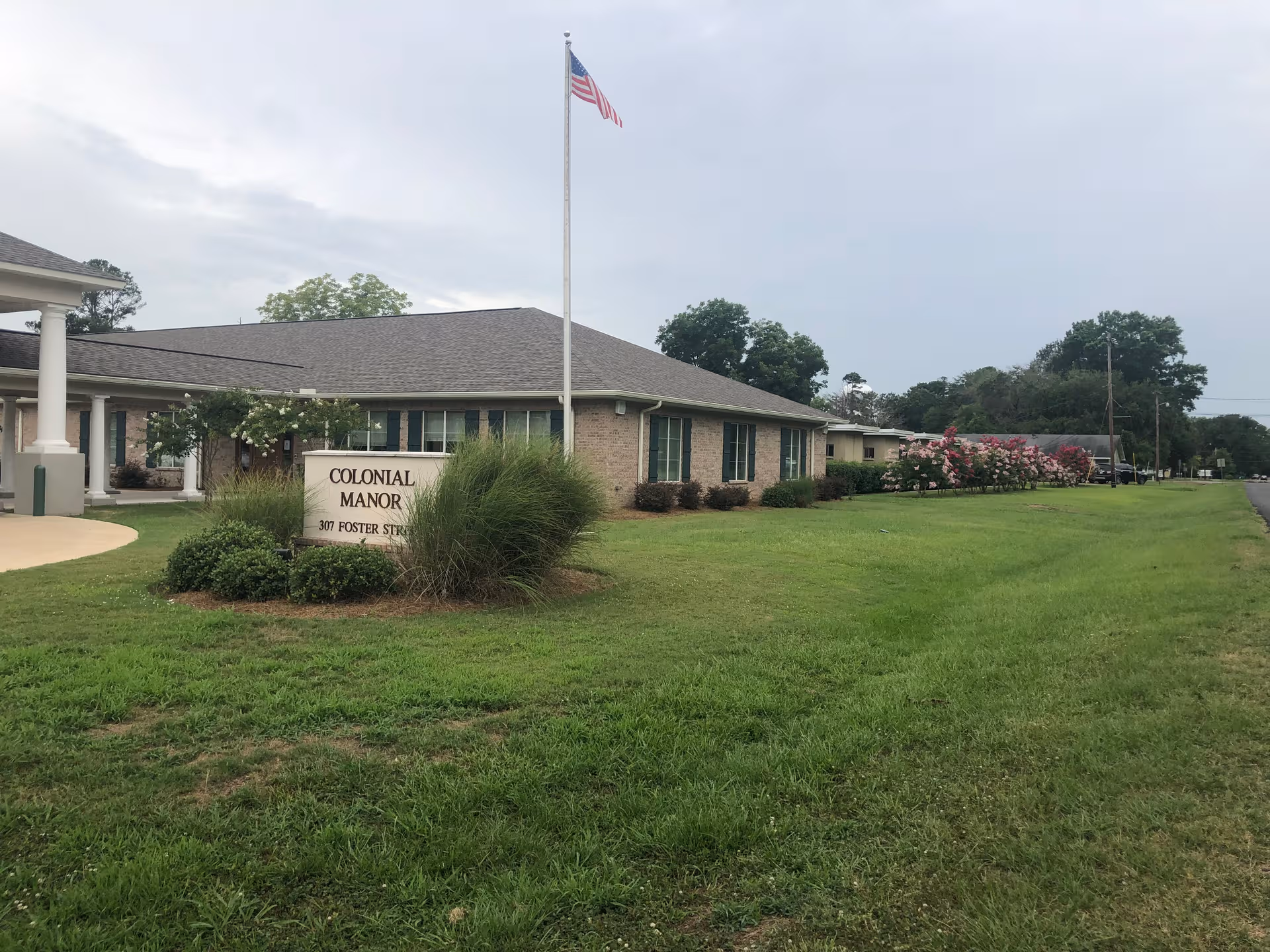 Exterior view of Colonial Manor Nursing & Rehab with sign, flagpole, and manicured lawn.
