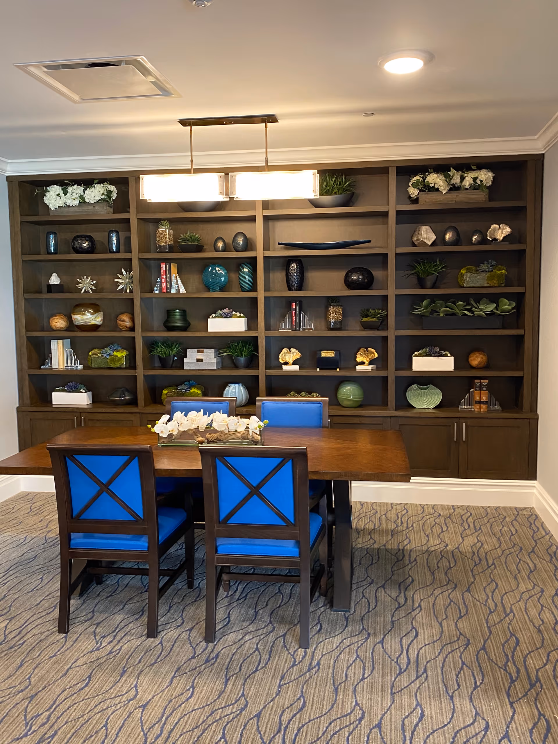 Well-lit dining area with dark wood bookshelf, table, and blue-cushioned chairs