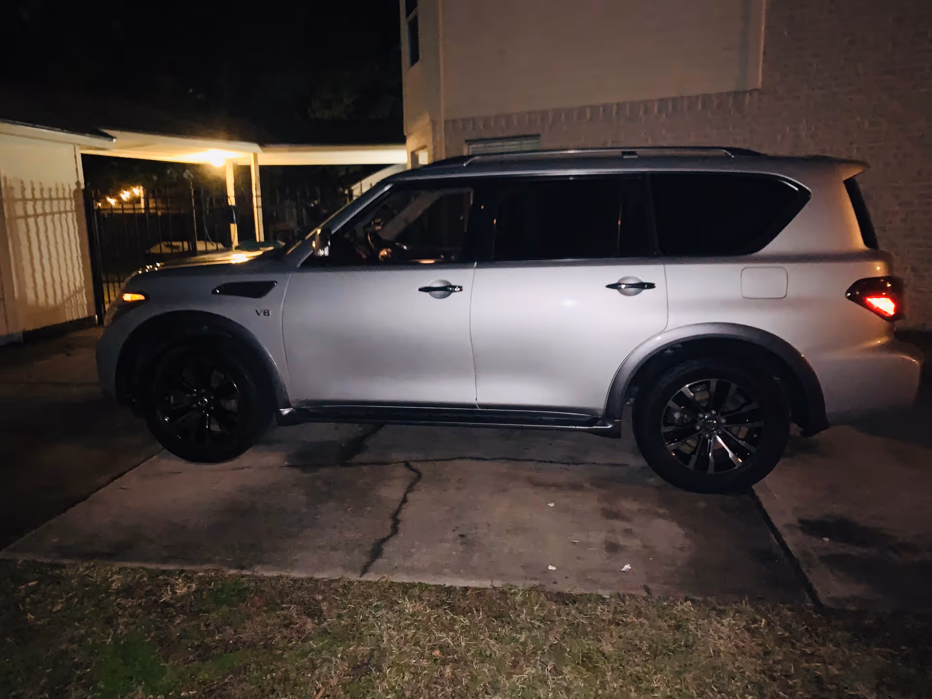 Silver SUV parked on a driveway beside a building at night under exterior lights.