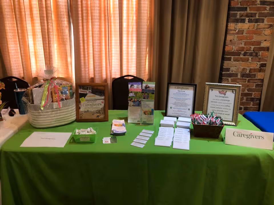 An information table for TLC Caregivers with brochures and certificates in a brick-walled room.