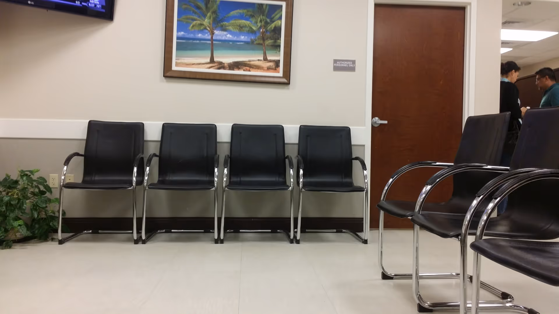 Lobby seating area with black chairs, plant, wall art, and a doorway in a clinic-like corridor.