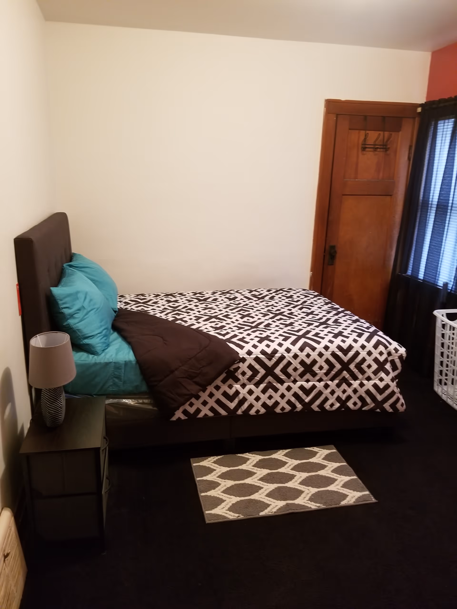A compact bedroom with a bed, nightstand, lamp, rug, and closet door.