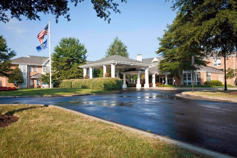 Front entrance of Our Lady of Hope Health Center showing a covered porte-cochere, flagpoles, wet driveway, and landscaped grounds.