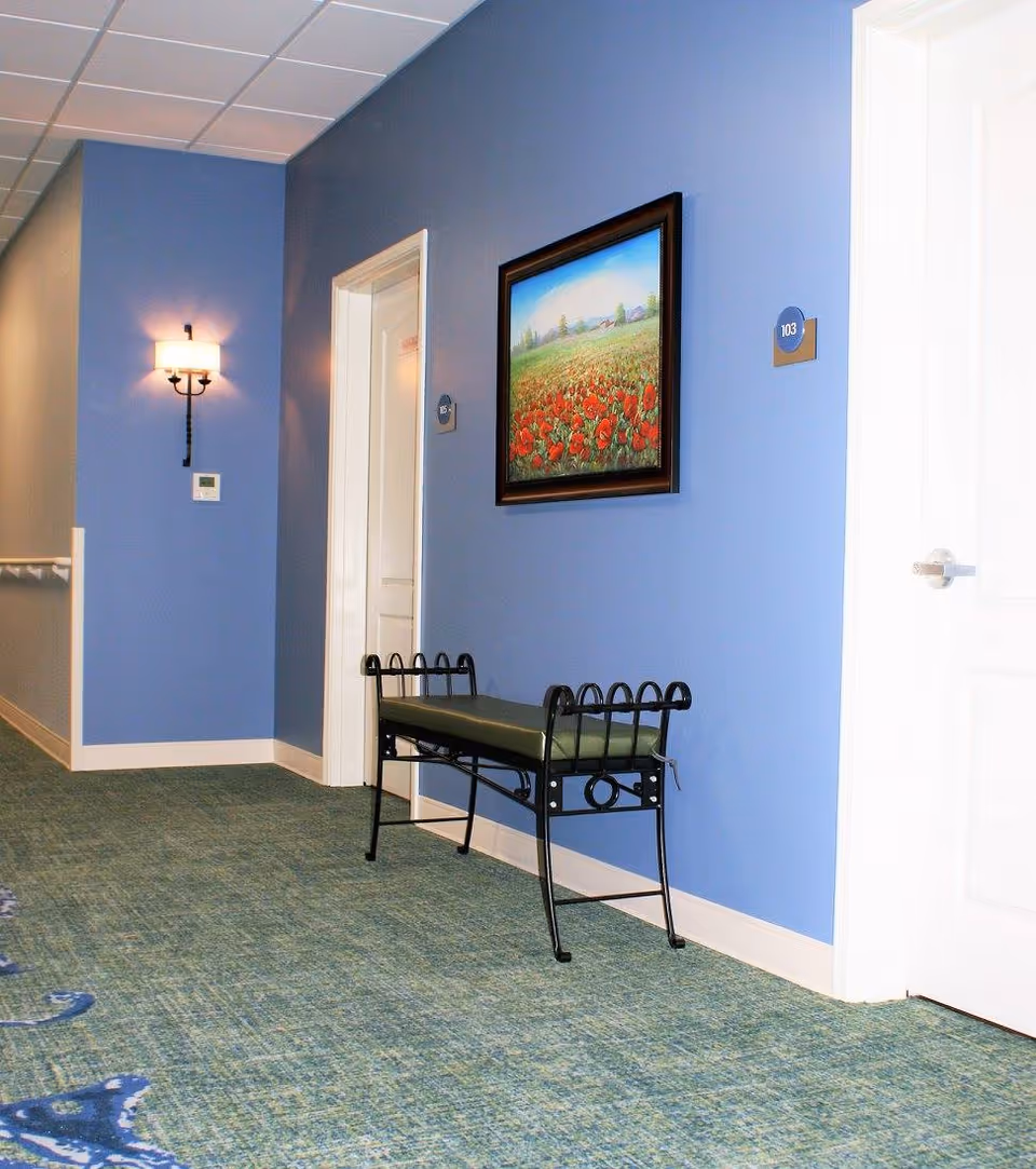 Blue hallway in Kinwell at South Lyon with painting, bench, and white doors.