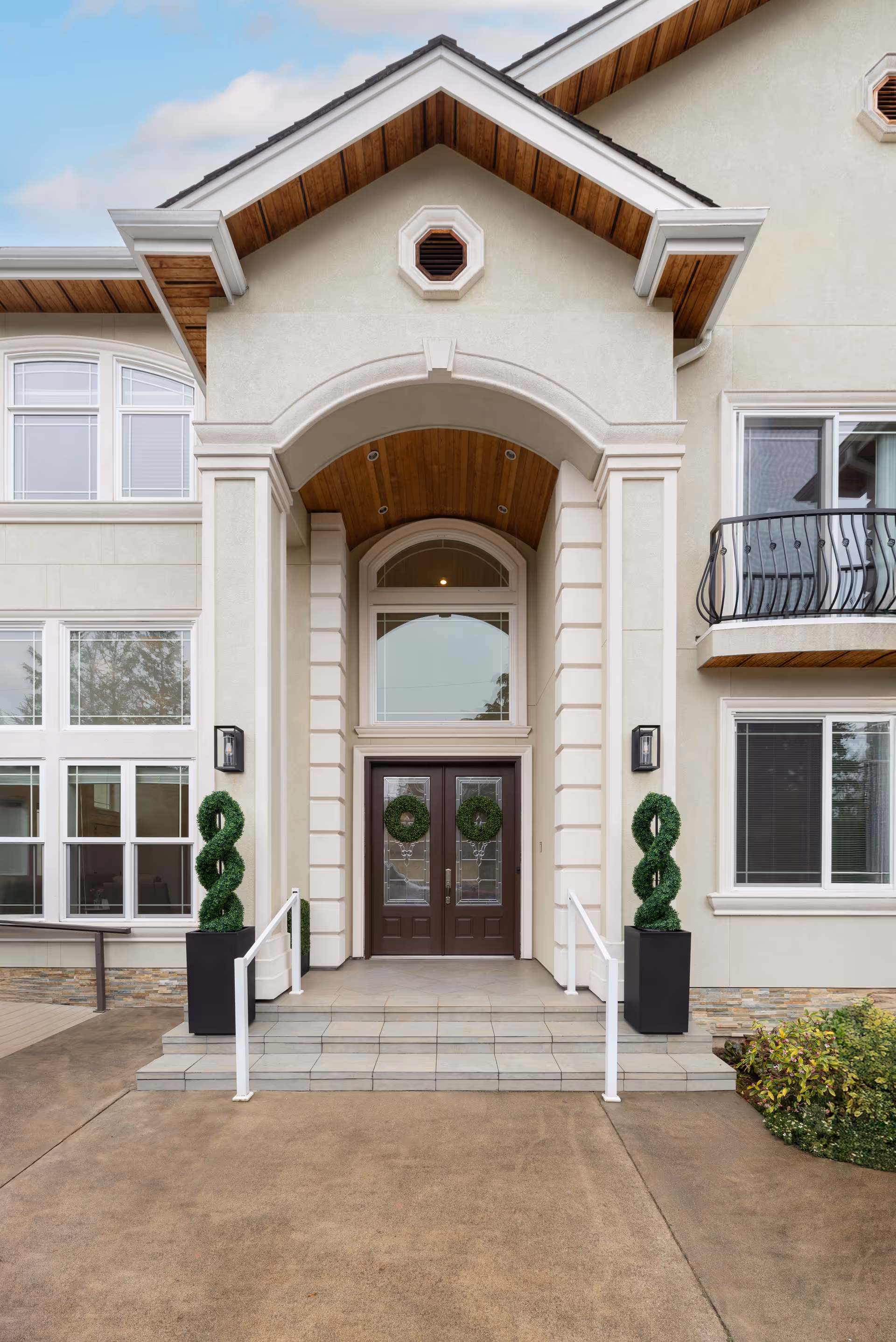 Front entrance of a beige senior living building with arched doorway and wreaths.