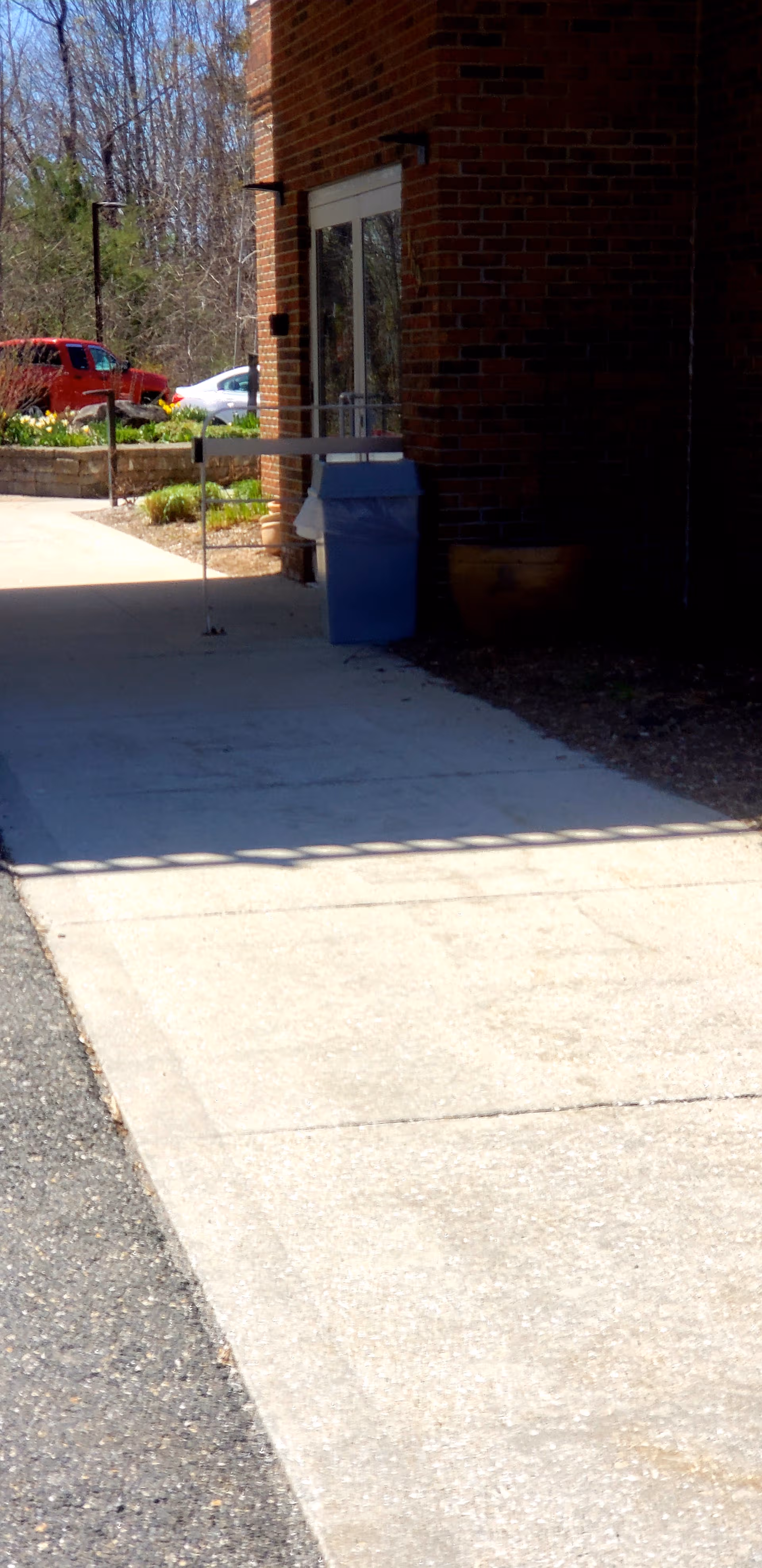 View of brick building entrance with glass doors, walkway, and parked cars nearby.