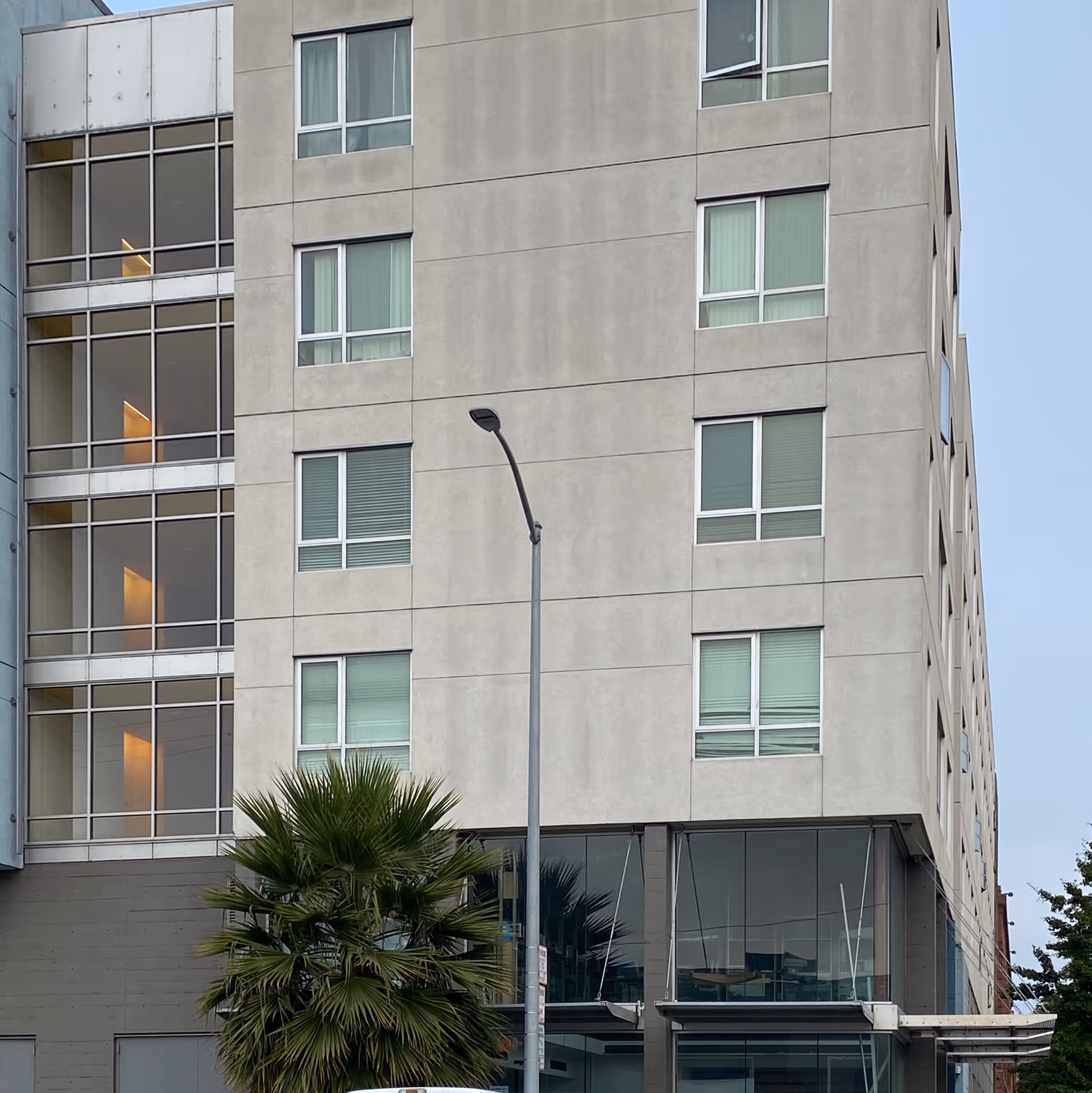 A multi-story concrete building exterior with large windows and a glass entrance, street lamp in front.