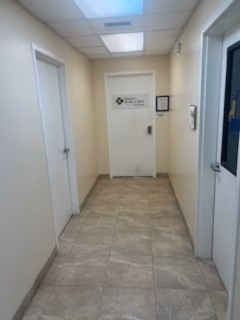 A clean hallway with doors on both sides leads to a closed door with a sign.