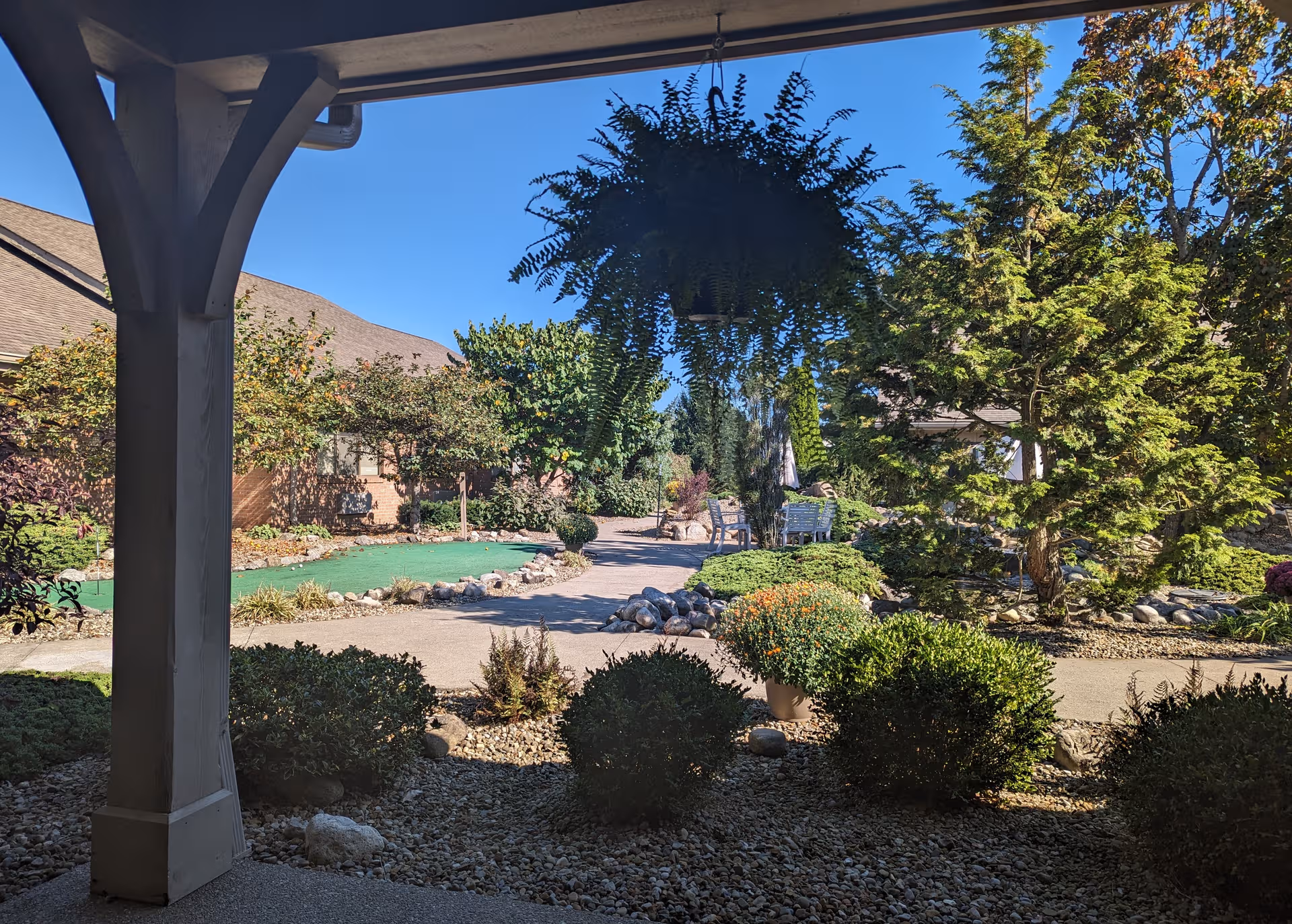 Sunny senior living courtyard with plants, a winding path, rocks, and seating under a covered patio.