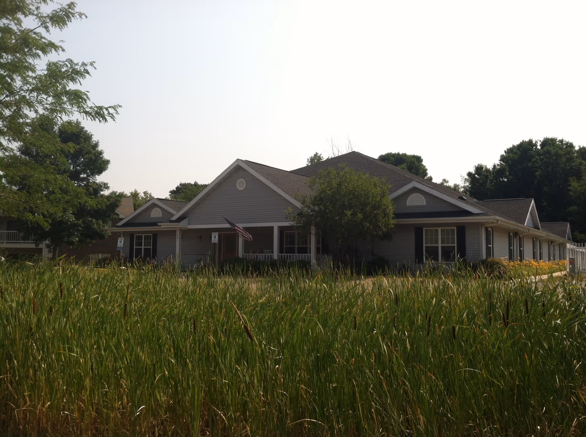 Front exterior of a single-story assisted living facility with a gabled roof and tall grasses.