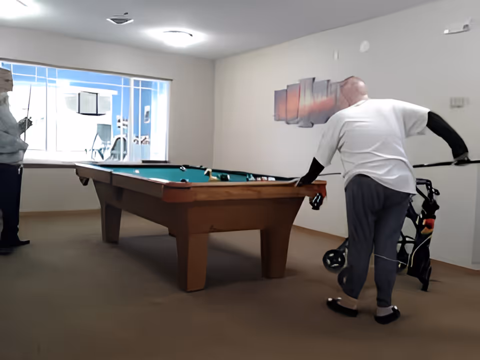 Two residents playing pool at a billiards table in a recreation room.
