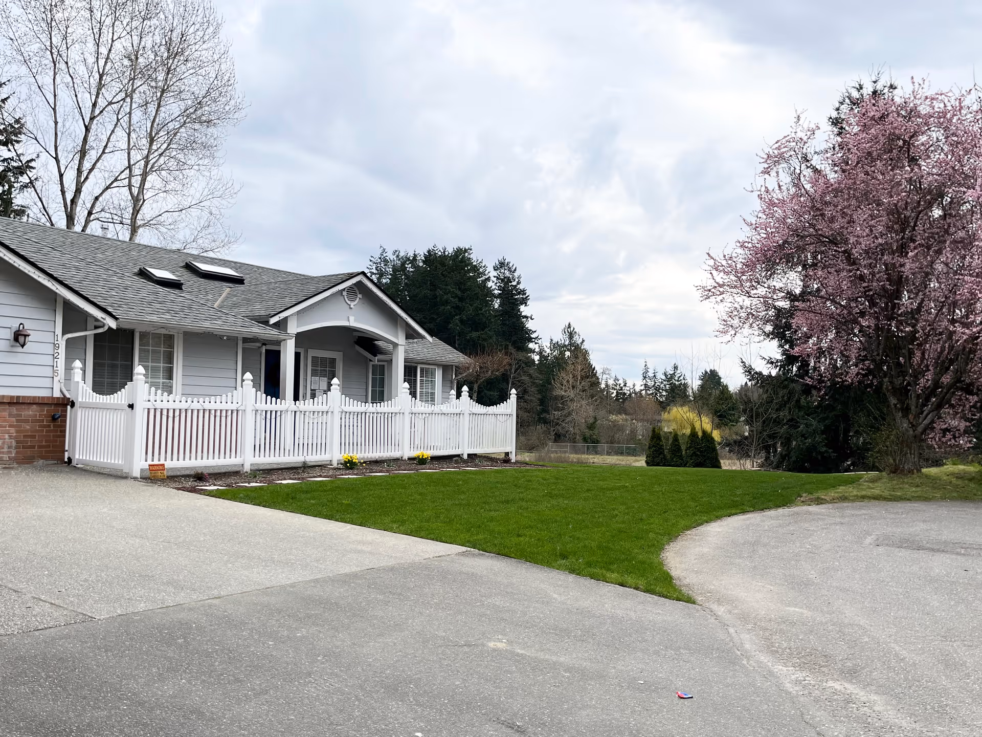 Single-story senior living facility with white fence, front porch, and blooming pink tree.