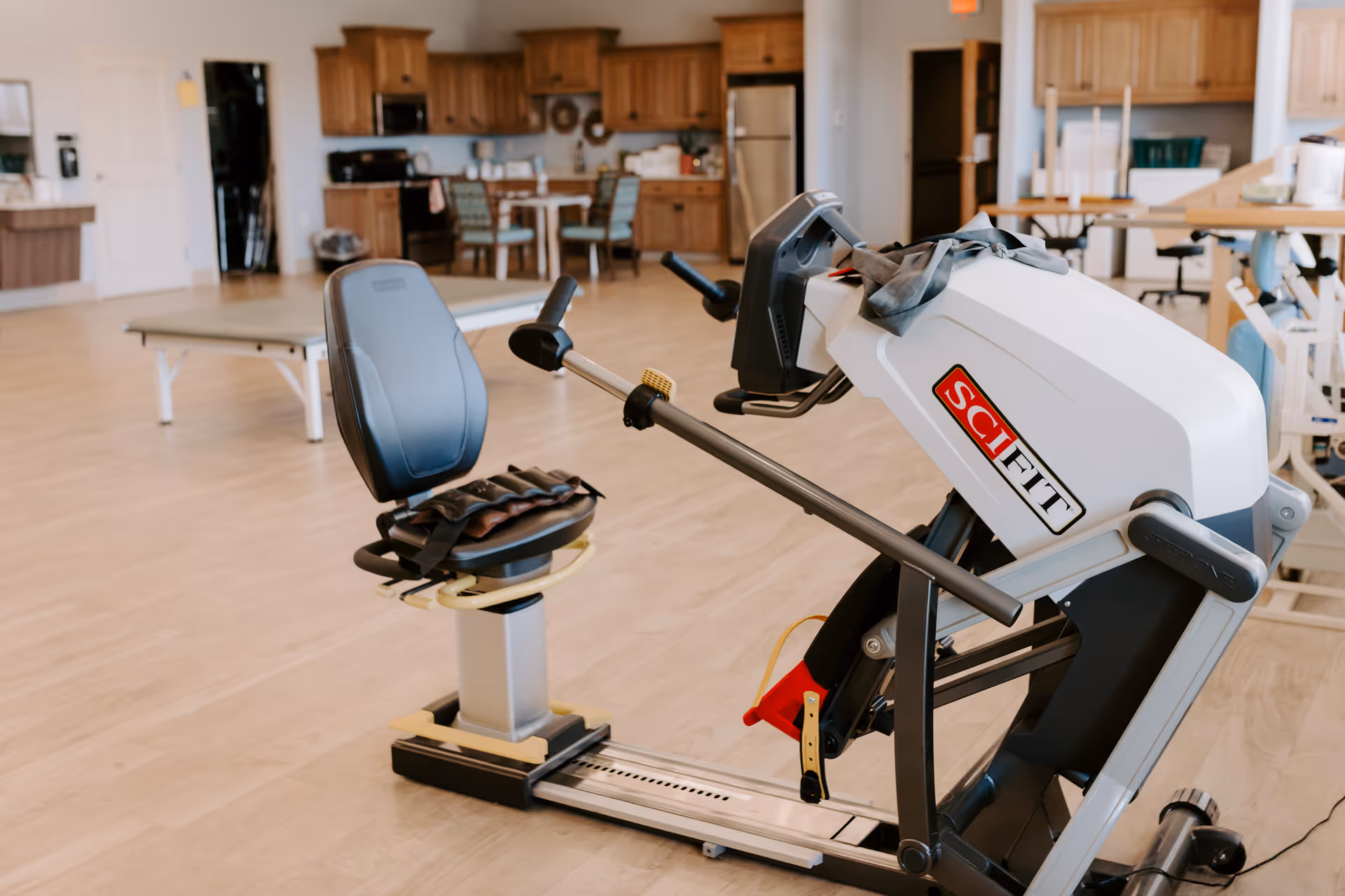 Exercise equipment in a spacious senior living common area with a kitchen in the background.