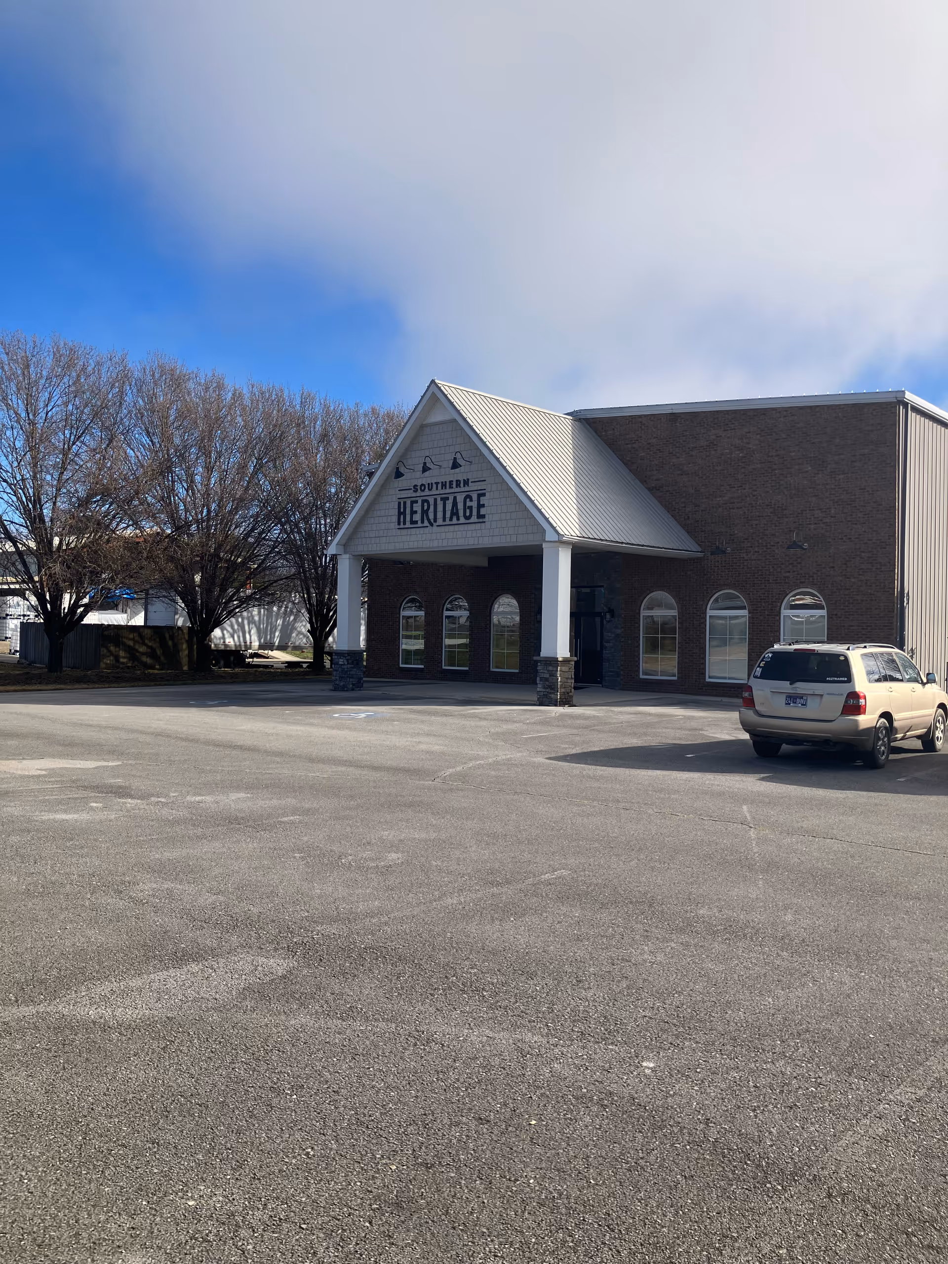 Exterior view of a brick senior care building with a peaked entry and parked car.