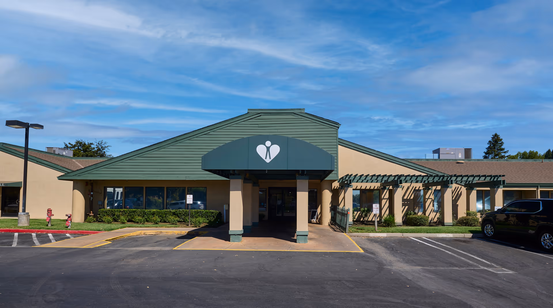 Front entrance of a single-story nursing and rehabilitation center with a green awning, drive-up canopy, and parking lot.