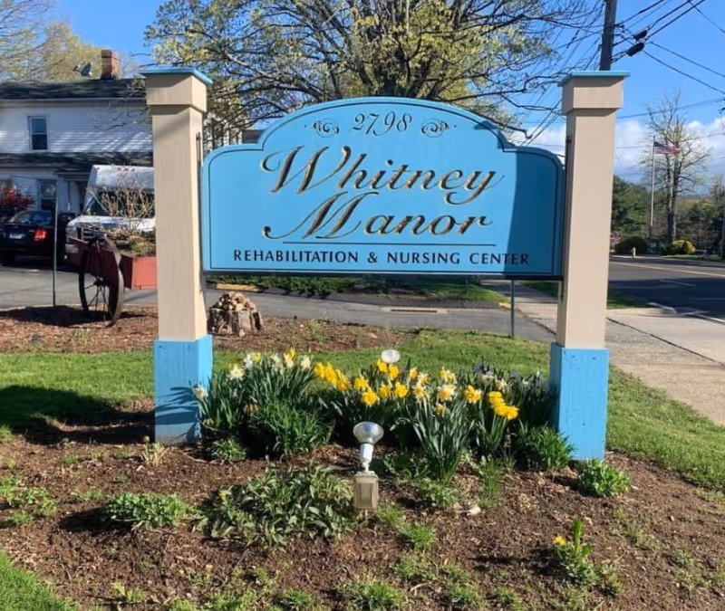 Whitney Manor Rehabilitation and Nursing Center sign sits in front with blooming flowers.
