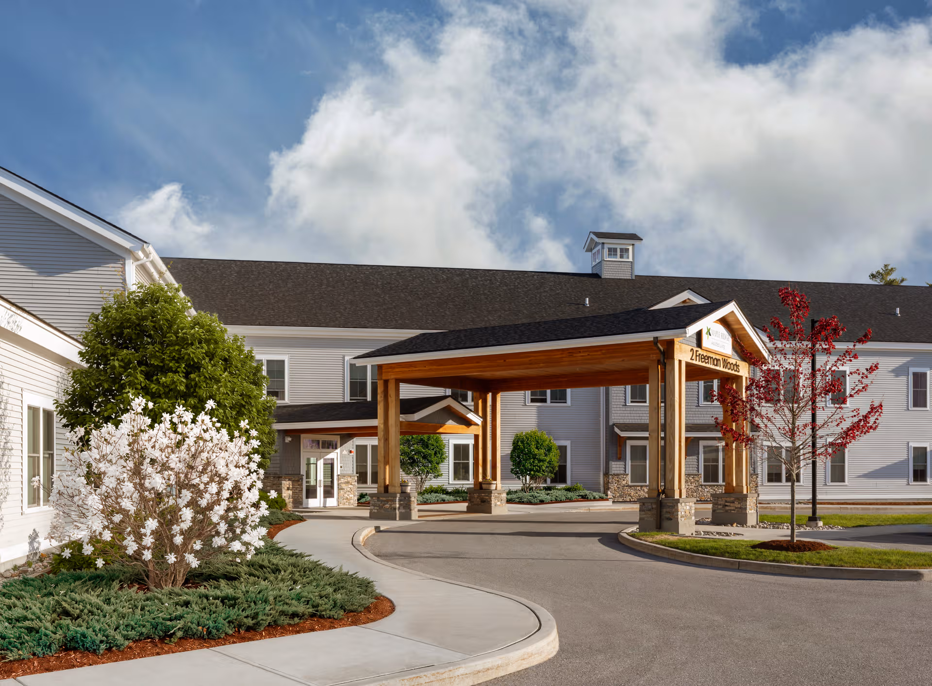 Exterior view of Maple Ridge Memory Care with a wooden covered entrance and landscaped surroundings.