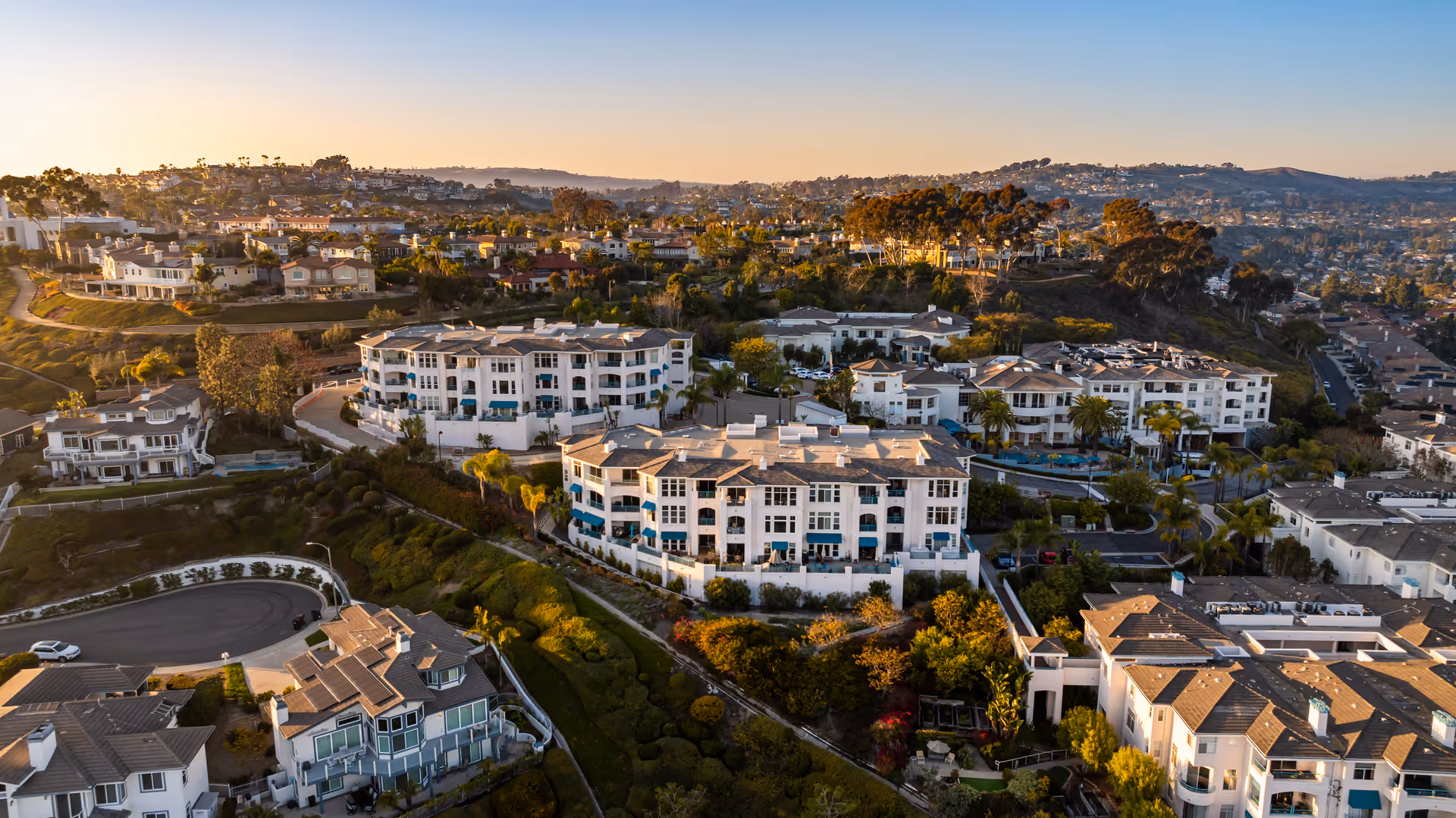 Aerial view of a coastal senior living complex and surrounding residential neighborhood at sunset.