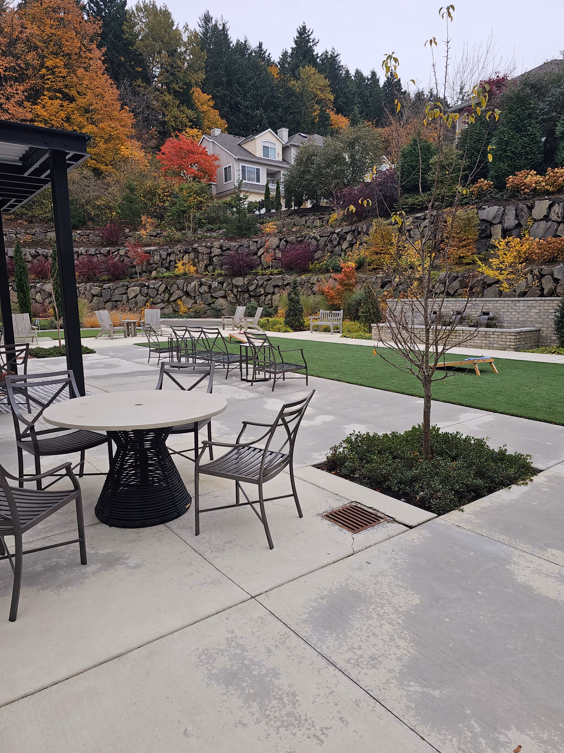 Outdoor patio area with metal tables and chairs, stone wall, and autumn trees.