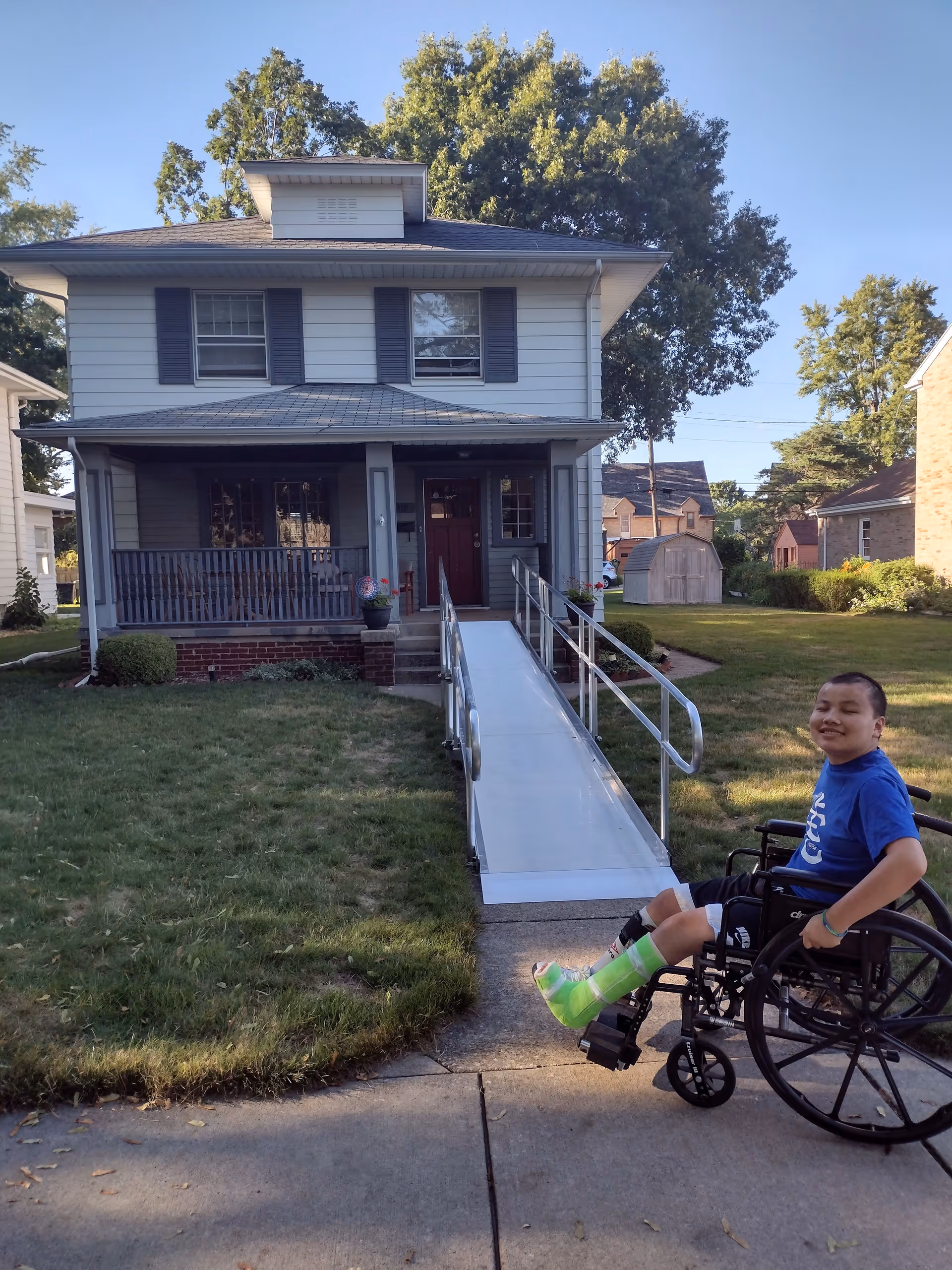 A two-story house with a ramp; a smiling person in a wheelchair sits nearby.