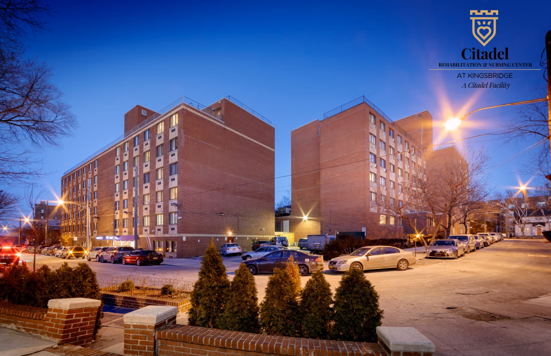 Exterior view of a brick senior living facility with two towers and parked cars.