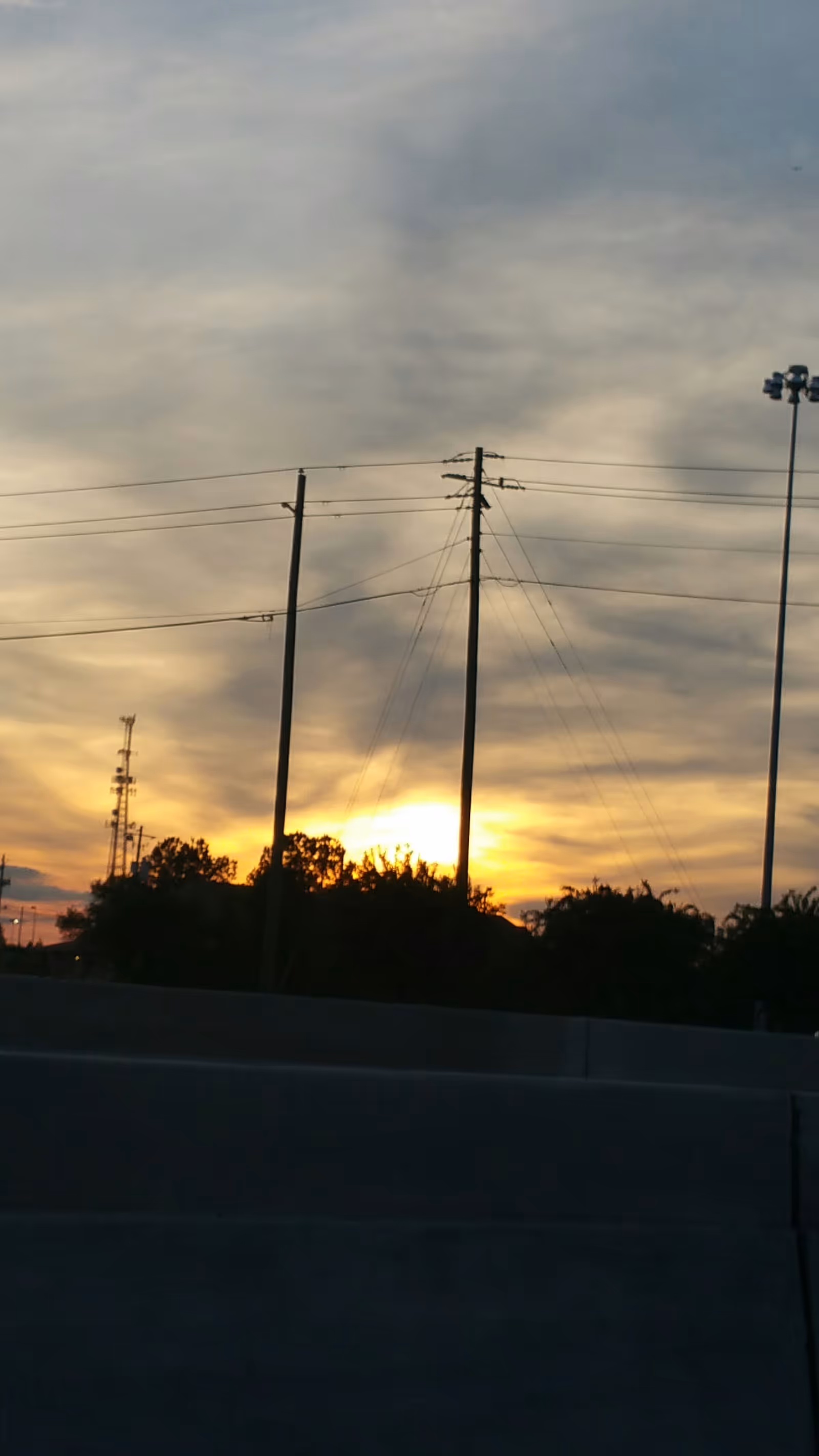 Sunset over a highway with power lines and silhouetted trees.