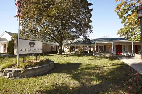 Exterior view of Golden Gardens in Milwaukee, sign and entry walkway with lawn and trees.