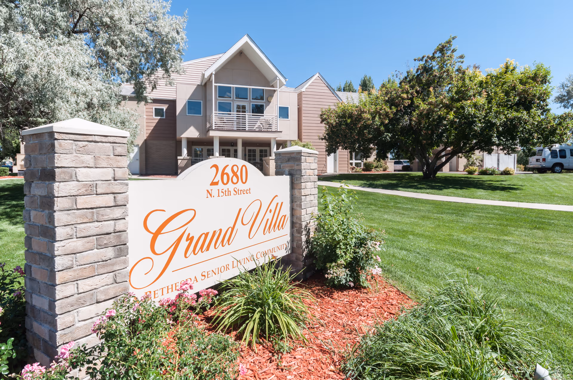 Two-story assisted living building with a large Grand Villa sign and well-kept lawn.