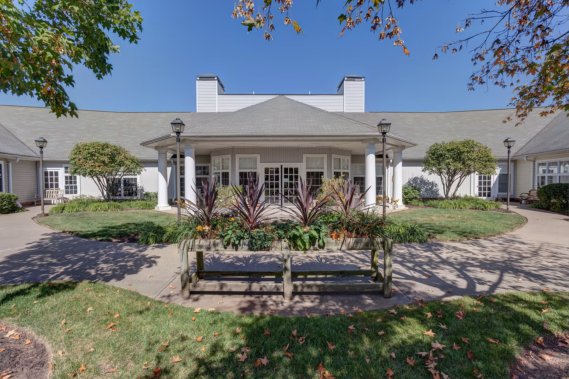 Front entrance of a healthcare facility with columns, landscaping, and a wooden bench.