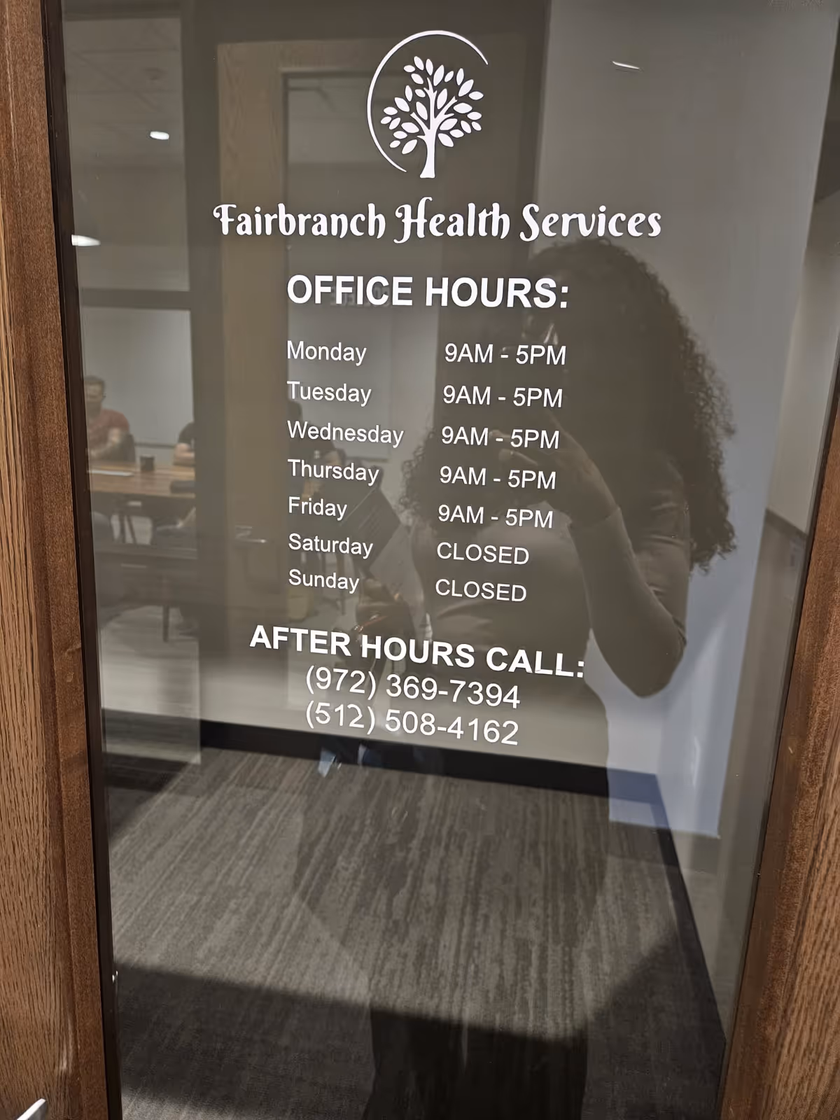 Glass door shows Fairbranch Health Services sign with office hours; hallway and seating visible.
