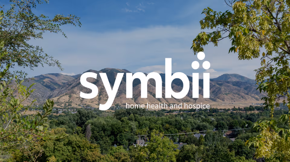 Scenic outdoor landscape with trees and mountains, overlaid by the Symbii Home Health & Hospice logo.