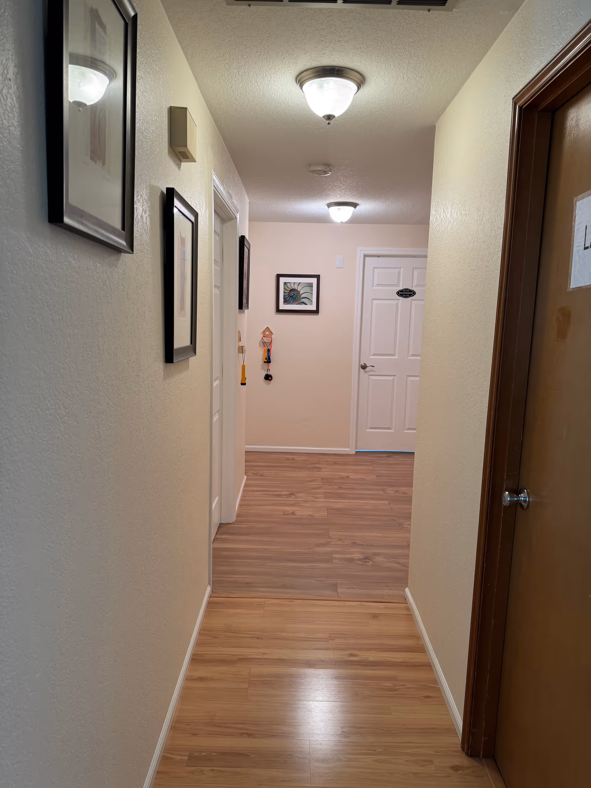Long hallway inside Elaine Gardens Adult Family Home with framed pictures and doors.