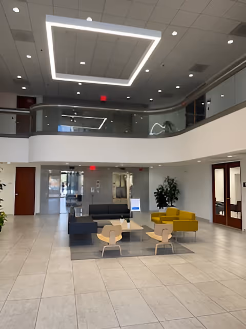 Spacious modern lobby with colorful seating, tables, potted plants, and an upper-level railing.