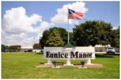 Lawn with Eunice Manor sign, American flag, trees, and cars in background.