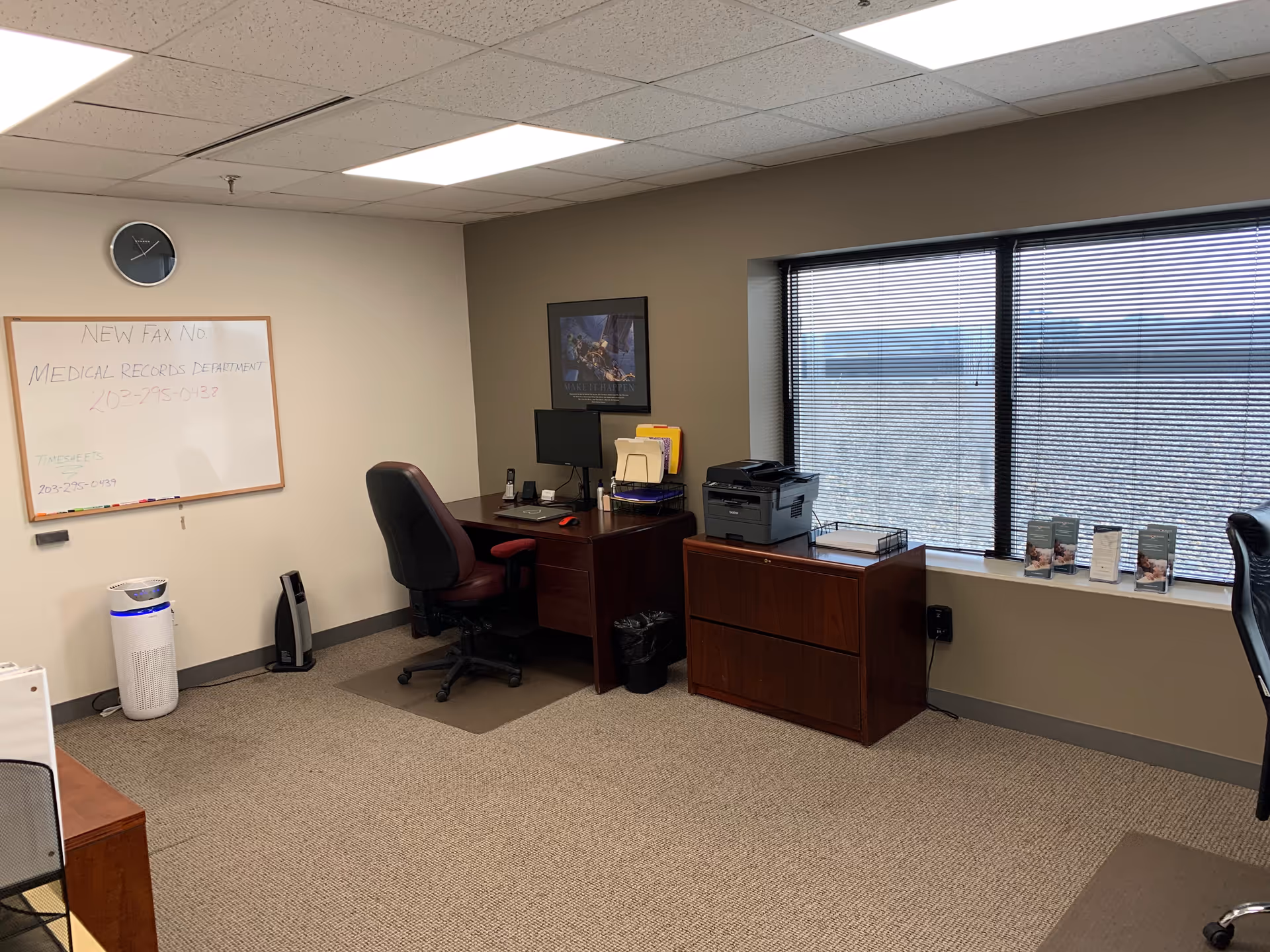 Office workspace with desk, computer, printer, filing cabinet, and large window blinds.