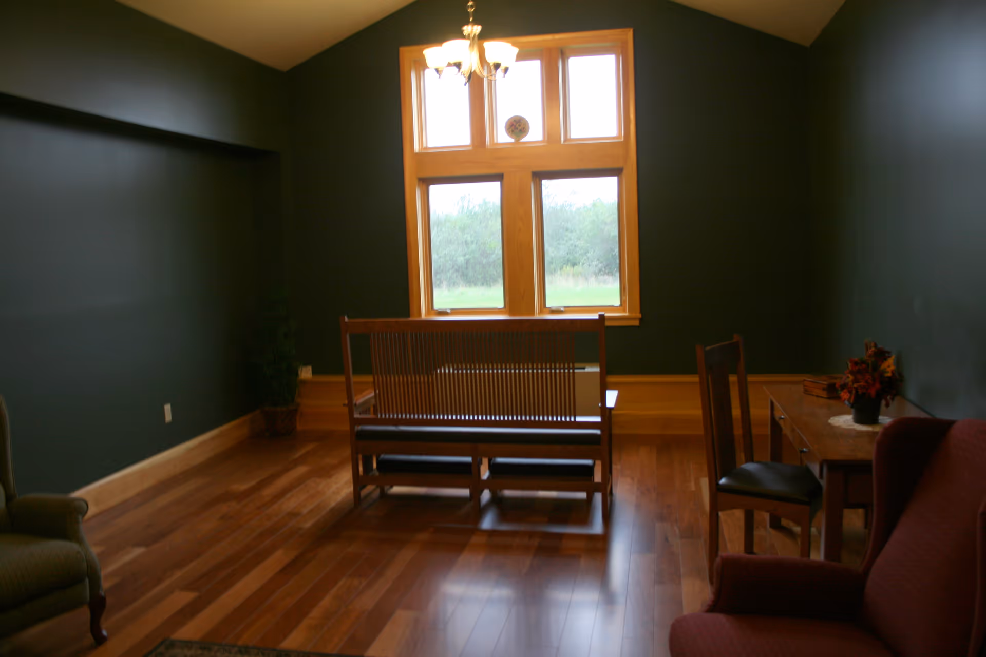 Cozy, empty living room with dark teal walls, hardwood floors, and window seating.