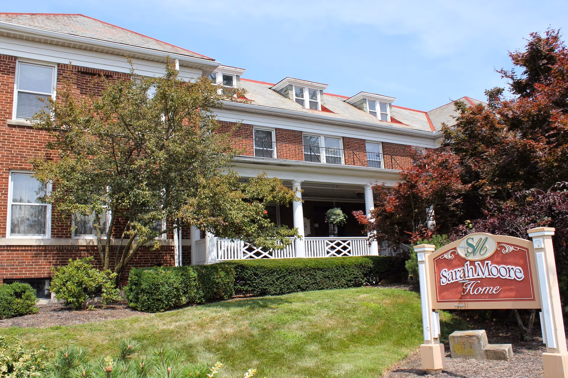 Brick senior living building with white porch, trees, and Sarah Moore Home sign.