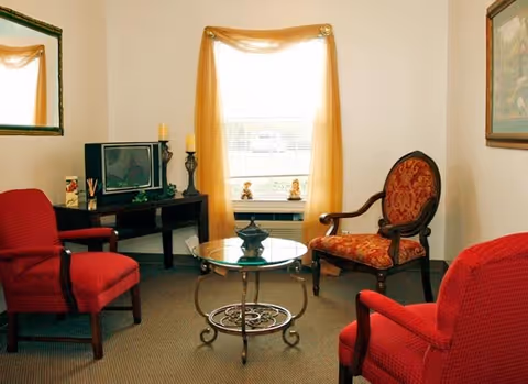 Interior living room with red chairs, glass coffee table, TV, and window with cream curtains.