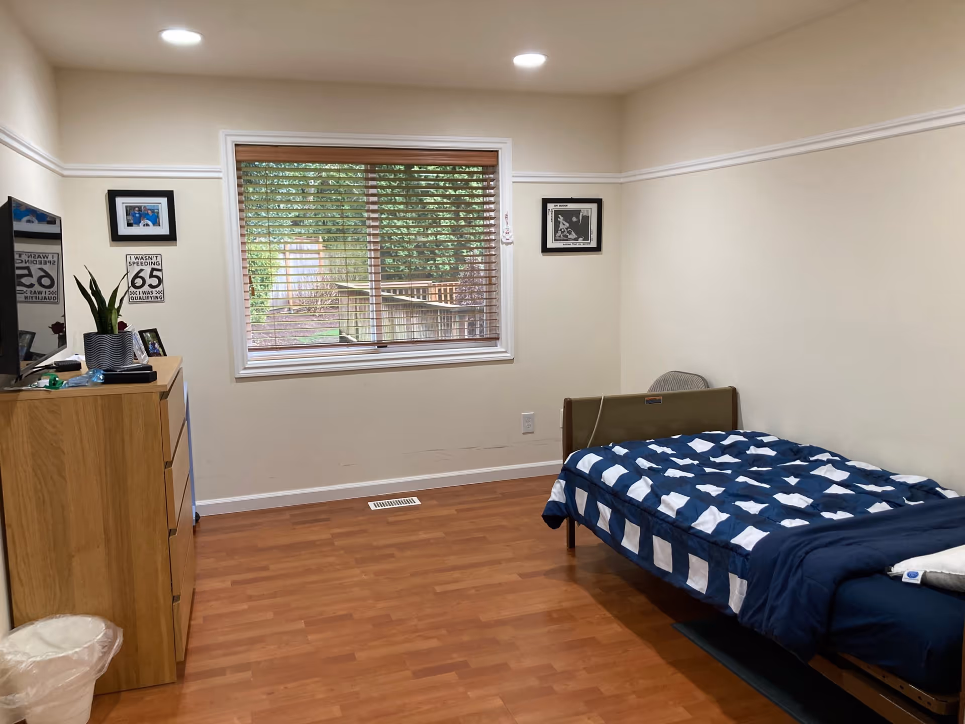 Senior living bedroom with bed, dresser, window blinds, and blue checkered bedding.