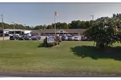 Exterior view of Autumn Care of Suffolk with parking lot, flagpole, and grassy lawn.