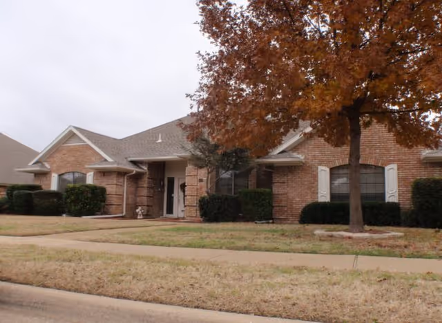Brick senior living facility front entrance with tree and sidewalk